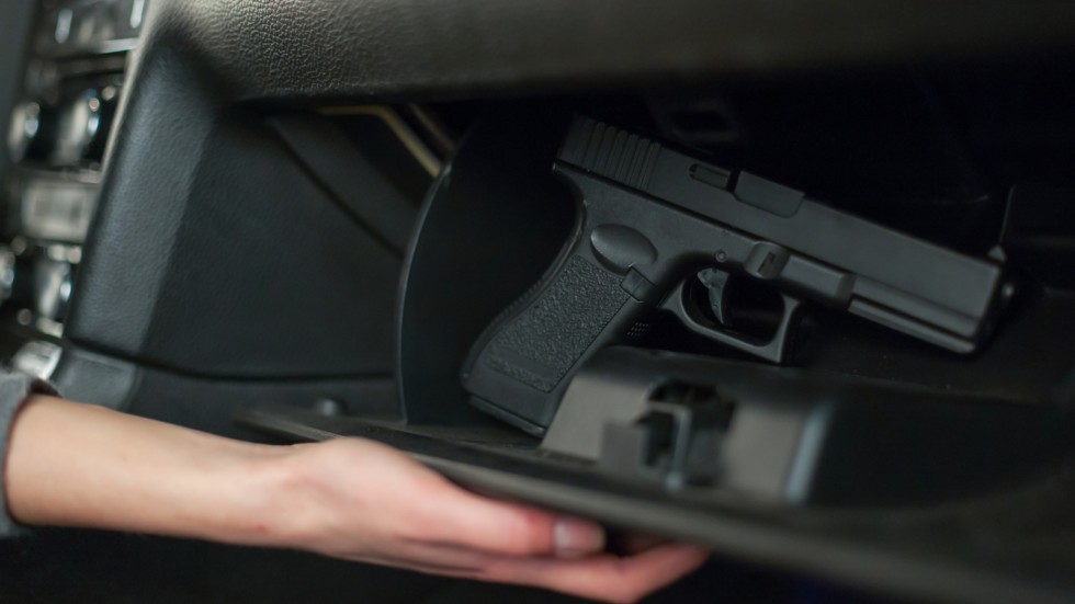 The female hand pulls out a gun from the glove box in the car.